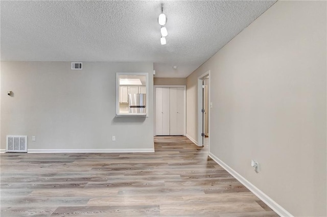 spare room featuring visible vents, baseboards, wood finished floors, and a textured ceiling