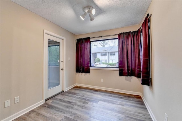 unfurnished room with baseboards, wood finished floors, and a textured ceiling