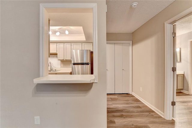 kitchen featuring baseboards, a sink, freestanding refrigerator, light wood-style floors, and a textured ceiling