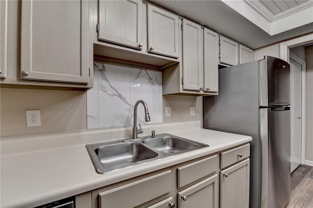 kitchen featuring a sink, light countertops, freestanding refrigerator, wood finished floors, and decorative backsplash