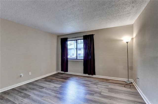 spare room featuring baseboards, a textured ceiling, and wood finished floors