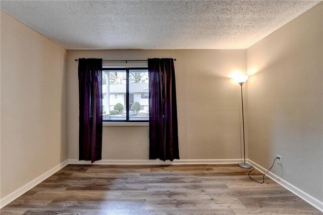 empty room featuring a textured ceiling, baseboards, and wood finished floors