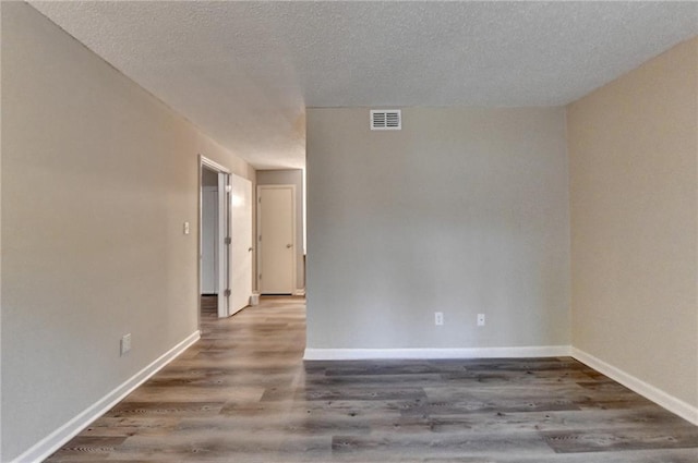 empty room with a textured ceiling, wood finished floors, baseboards, and visible vents
