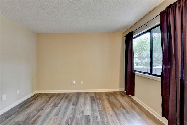 empty room with baseboards, wood finished floors, and a textured ceiling