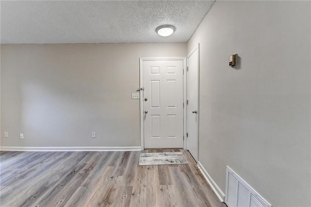 interior space with visible vents, a textured ceiling, baseboards, and wood finished floors