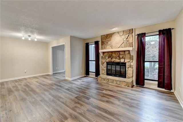 unfurnished living room featuring a stone fireplace, baseboards, wood finished floors, and a textured ceiling