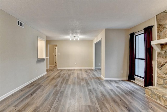 unfurnished living room with visible vents, a textured ceiling, baseboards, and wood finished floors