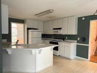 kitchen featuring white appliances, a peninsula, a breakfast bar, light countertops, and light tile patterned floors