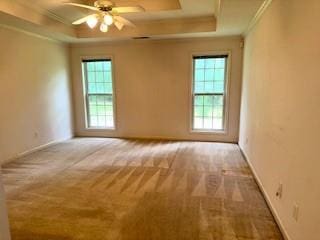 carpeted spare room featuring a tray ceiling, plenty of natural light, crown molding, a ceiling fan, and baseboards