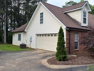 view of home's exterior with concrete driveway, a garage, brick siding, and central air condition unit