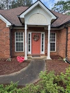 property entrance featuring brick siding and a shingled roof