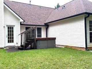 rear view of house with a hot tub, a yard, and roof with shingles