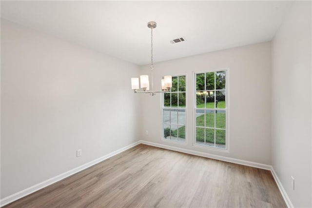 empty room with wood finished floors, visible vents, baseboards, and an inviting chandelier