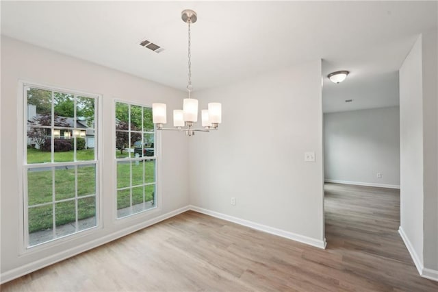 unfurnished dining area featuring visible vents, baseboards, wood finished floors, and a notable chandelier