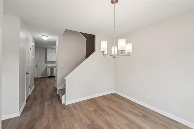 unfurnished dining area featuring stairway, an inviting chandelier, wood finished floors, and baseboards