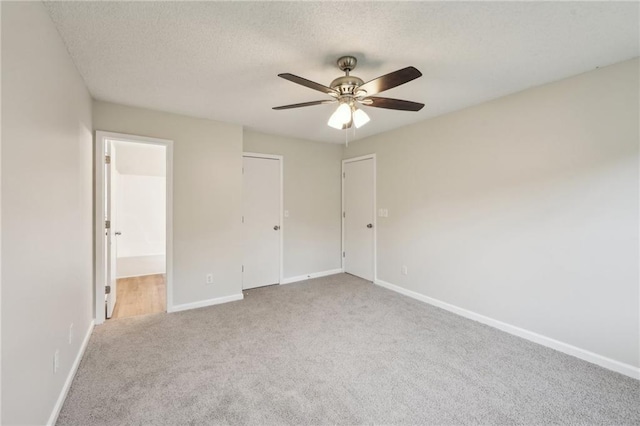 unfurnished bedroom with a ceiling fan, a textured ceiling, carpet floors, baseboards, and ensuite bath