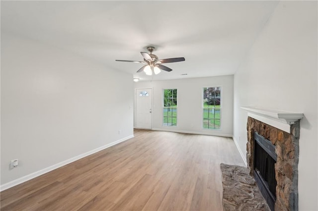 unfurnished living room featuring light wood-type flooring, baseboards, a ceiling fan, and a stone fireplace