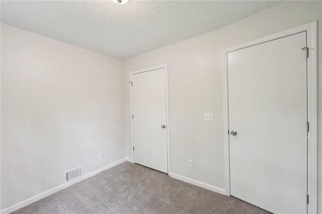 unfurnished bedroom featuring a textured ceiling, carpet, visible vents, and baseboards