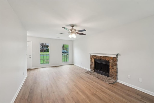 unfurnished living room featuring wood finished floors, a ceiling fan, baseboards, and a stone fireplace