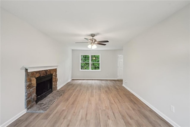 unfurnished living room with baseboards, a stone fireplace, wood finished floors, and ceiling fan