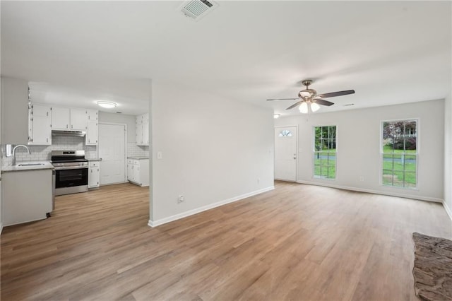 unfurnished living room with visible vents, light wood finished floors, ceiling fan, and a sink