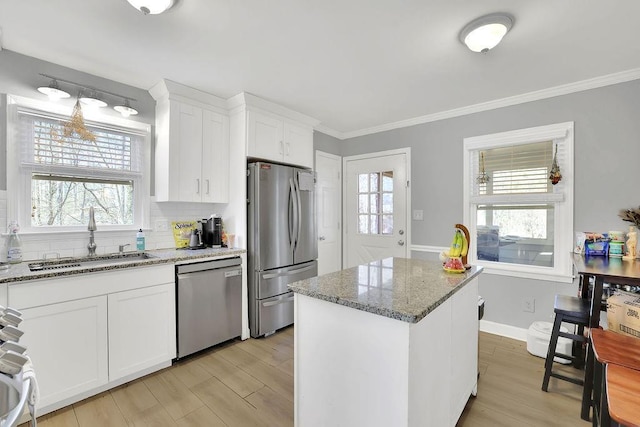 kitchen featuring white cabinets, stainless steel appliances, light stone counters, a kitchen island, and sink