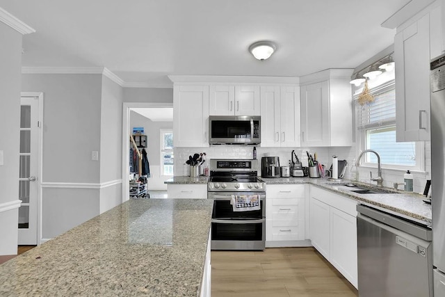 kitchen with appliances with stainless steel finishes, ornamental molding, light stone counters, white cabinets, and sink