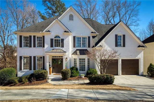 view of front of home with french doors, concrete driveway, an attached garage, a shingled roof, and brick siding