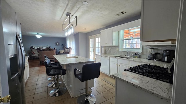 kitchen featuring stainless steel refrigerator with ice dispenser, white dishwasher, white cabinets, a kitchen island, and decorative light fixtures