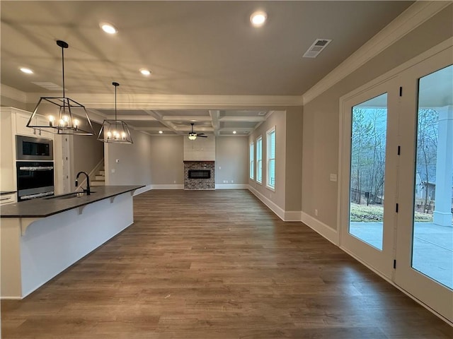 kitchen with pendant lighting, sink, stainless steel microwave, white cabinets, and a brick fireplace