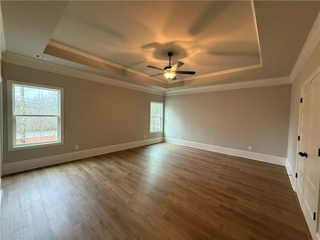 empty room with dark hardwood / wood-style flooring, a tray ceiling, ornamental molding, and ceiling fan