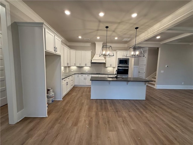 kitchen featuring stainless steel microwave, custom range hood, an island with sink, white cabinets, and oven