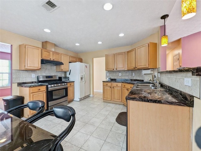 kitchen featuring pendant lighting, stainless steel gas range oven, light brown cabinets, white refrigerator with ice dispenser, and sink