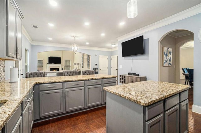 kitchen with gray cabinets, visible vents, dark wood-type flooring, a warm lit fireplace, and a peninsula