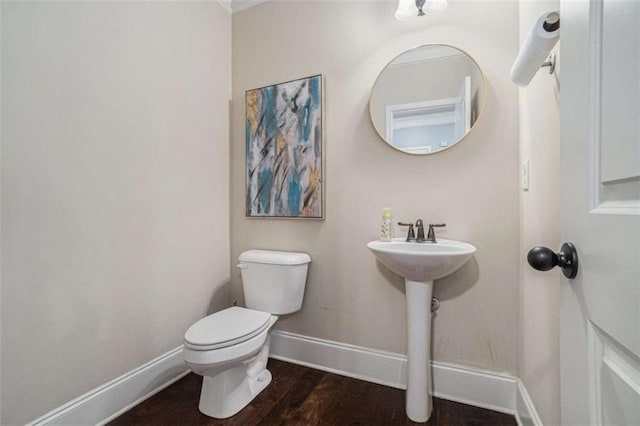 half bathroom with baseboards, toilet, and wood finished floors