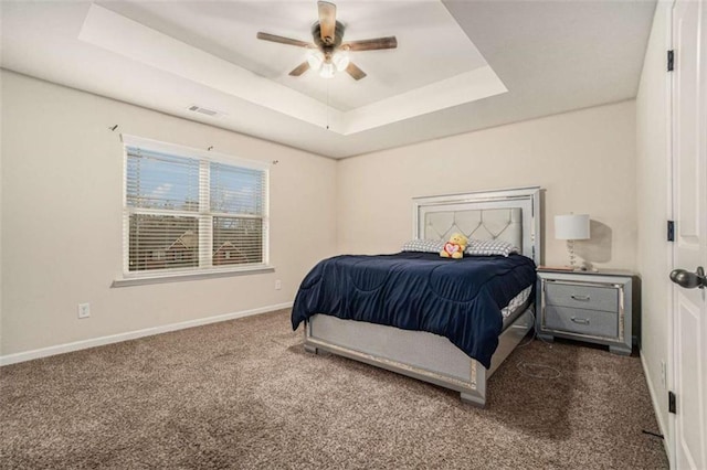 bedroom with a tray ceiling, visible vents, a ceiling fan, carpet flooring, and baseboards