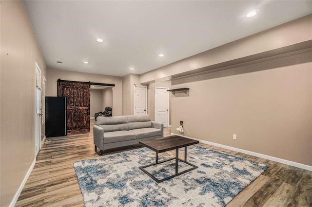 living room with a barn door, recessed lighting, wood finished floors, and baseboards