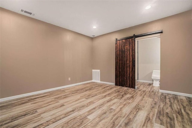 unfurnished room with wood finished floors, visible vents, baseboards, and a barn door