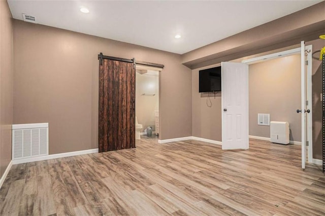 spare room with baseboards, a barn door, visible vents, and wood finished floors