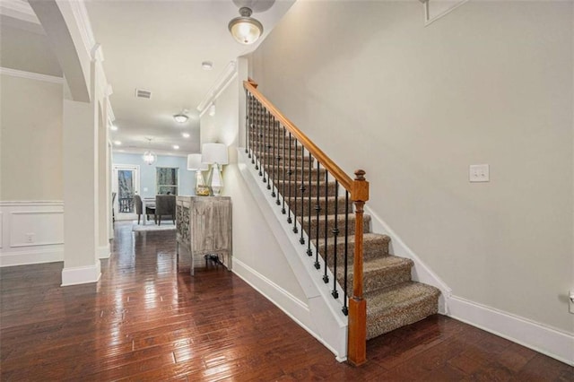 stairway with a decorative wall, wood-type flooring, visible vents, and crown molding