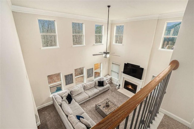 living area with baseboards, a fireplace with flush hearth, carpet flooring, and crown molding