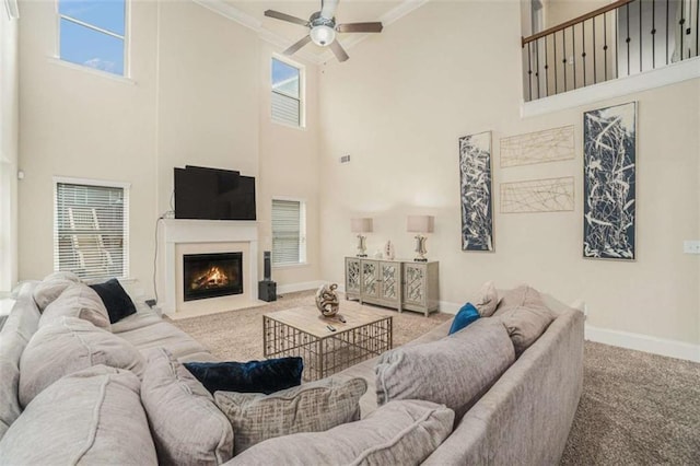 living room featuring carpet floors, crown molding, a fireplace with flush hearth, ceiling fan, and baseboards