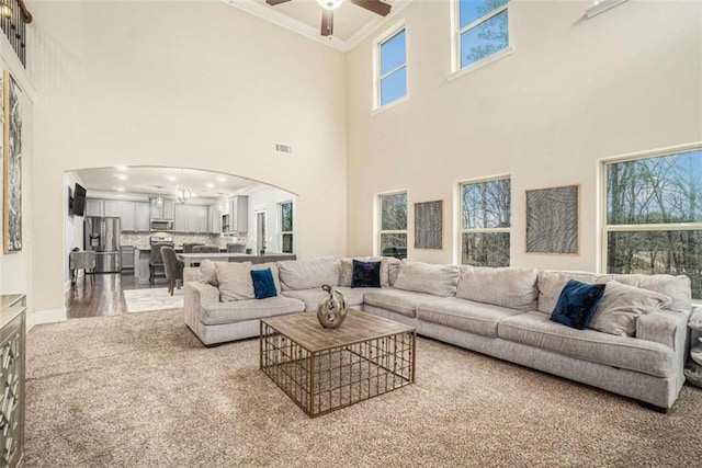 living area with ornamental molding, arched walkways, visible vents, and a ceiling fan