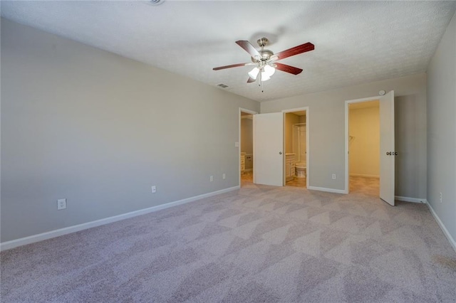 unfurnished bedroom with a closet, connected bathroom, ceiling fan, light carpet, and a walk in closet