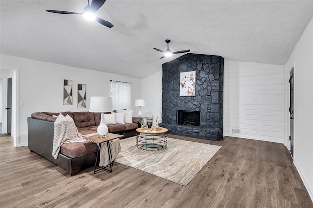 living room featuring a stone fireplace, ceiling fan, vaulted ceiling, and hardwood / wood-style flooring