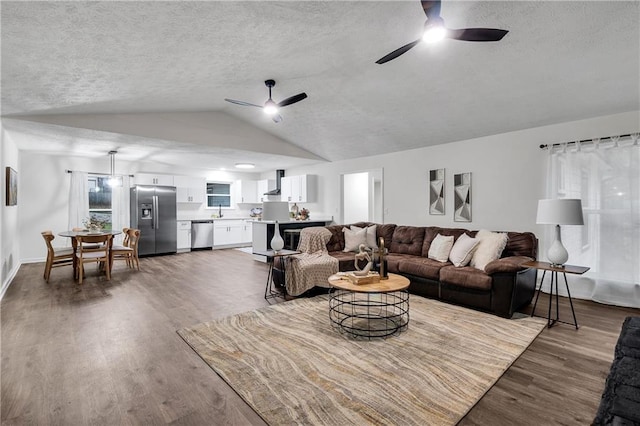 living room with a textured ceiling, ceiling fan, dark wood-type flooring, and vaulted ceiling