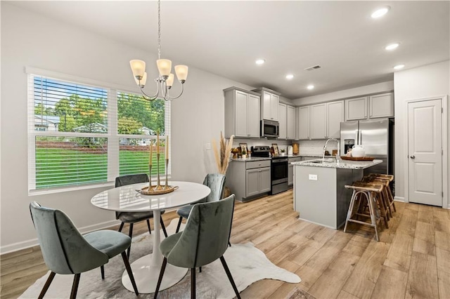 kitchen with gray cabinets, appliances with stainless steel finishes, decorative light fixtures, an island with sink, and light stone counters