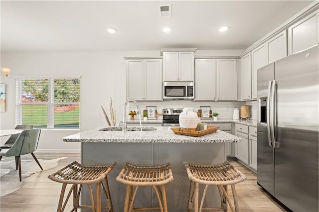 kitchen featuring sink, a kitchen island with sink, stainless steel appliances, a kitchen breakfast bar, and light stone counters