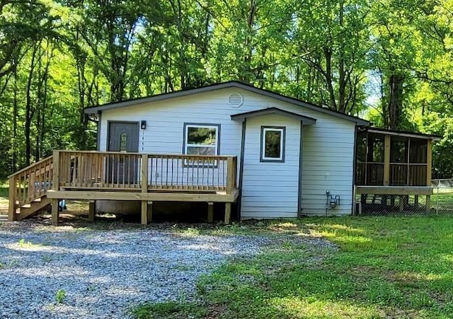 back of property with a sunroom, a deck, a lawn, and stairs