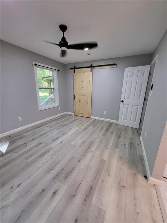 unfurnished bedroom with light wood finished floors, a barn door, baseboards, and ceiling fan